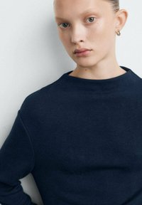 Felpa blu navy con collo alto, maniche lunghe e tessuto morbido e strutturato. Design semplice, dettagli minimalisti e silhouette aderente.