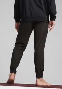 Pantalons de sport noirs avec une coupe ajustée et une texture douce, présentant un design effilé et une taille élastique, montrés de l'arrière avec des pieds nus.