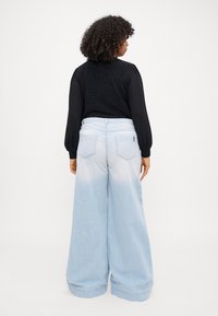 Lys blå vide jeans som falmer fra mørkere til lysere ved kanten, kombinert med en svart strukturert langermet topp.