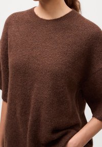Pull marron en maille avec manches courtes, col rond, texture douce et coupe décontractée, présentant une légère peluche sur toute la surface.