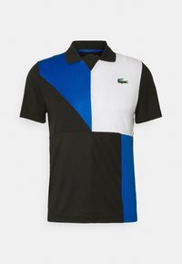 Polotröja i svarta, vita och blå färgblock, med krage, korta ärmar och en broderad grön krokodil-logotyp.