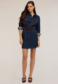 Denim jurk met een knoopsluiting, lange mouwen opgerold bij de cuffs, twee borstzakken en een bordeauxrode riem. Soepele textuur, donkerblauwe kleur.