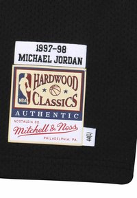 L'étiquette du maillot de sport noir présente "1997-98" et "Michael Jordan" en blanc au-dessus d'un logo coloré "Hardwood Classics" et de la signalétique.