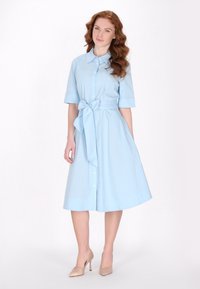 Hellblaues Hemdkleid aus Baumwolle. Mit Kragen, kurzen Ärmeln, einem Bindegürtel in der Taille und einem ausgestellt geschnittenen Rock, mit durchgehender Knopfleiste.