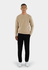 Beige ribbestrikket genser kombinert med svarte bukser og hvite sneakers. Genseren har rund hals og lange ermer.