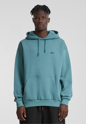 Felpa con cappuccio in teal, realizzata in tessuto morbido. Presenta una tasca frontale, polsini a costine e un piccolo logo nero sul petto.