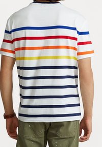 Camiseta de algodón blanca de manga corta con rayas horizontales en rojo, naranja, amarillo, azul y azul marino. Ajuste relajado con un diseño sencillo.