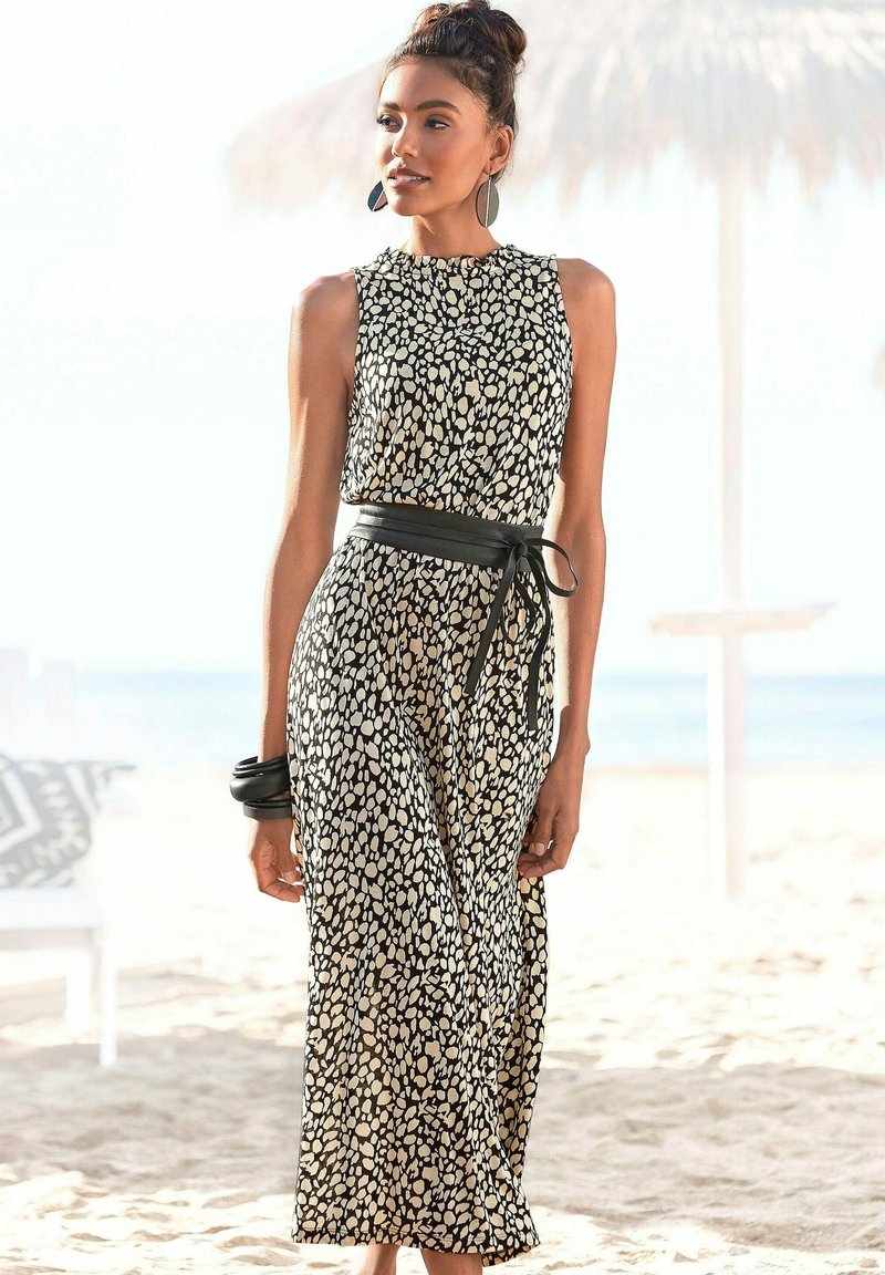 Czarna sukienka w białe kropki, bezrękawowy fason, z paskiem w talii i długości do połowy łydki. Noszona z czarnymi akcesoriami.