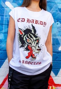Camiseta blanca de algodón con un gráfico negro y rojo de un tigre que muestra los colmillos, sosteniendo un hueso rojo en la boca, etiquetado como "ED HARDY LOS ÁNGELES".