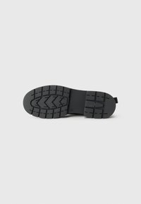 Black rubber shoe sole with a patterned tread, featuring zigzag grooves and a flat heel. Simple design, smooth texture, and durable material.