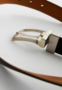Cinturón de cuero negro con un acabado suave, que presenta una hebilla metálica plateada de forma rectangular y textura cepillada. Se pueden ver costuras de contraste.