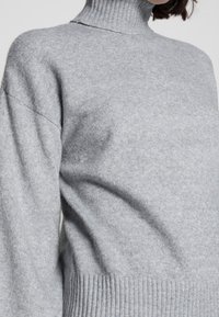 Grauer Rollkragenpullover aus weichem Strickstoff, mit einem gerippten Kragen und Saum, in lockerer Passform und mit überschnittenen Schultern.