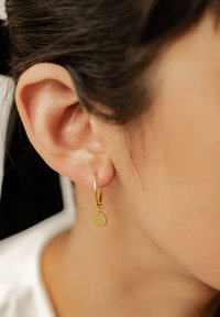 Orecchino a cerchio in oro con un piccolo ciondolo circolare che presenta un design a occhio, appeso allobo dell'orecchio, con una finitura liscia e lucida.