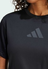 Melnā sporta t-kreklā no gludas auduma, ar apaļu kakla izgriezumu un matētu tumšu logotipa dizainu priekšpusē. Īsas piedurknes.