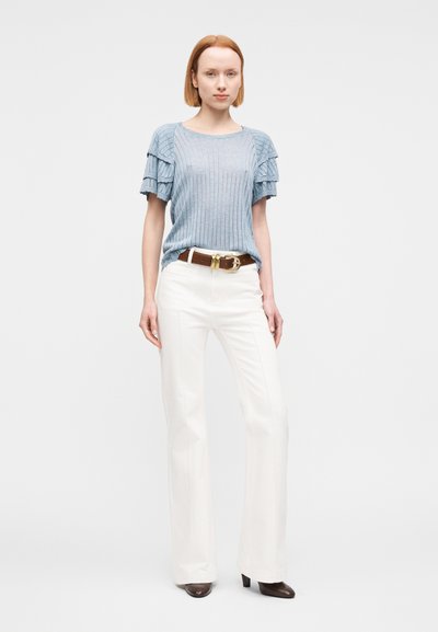 Haut en maille côtelée bleu clair avec manches courtes volantées, associé à un pantalon blanc évasé et une ceinture marron avec une boucle dorée.