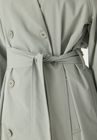 Ljusgrön, dubbelknäppt trenchcoat med bälte i midjan, med stora knappar och ett slätt, strukturerat tyg.