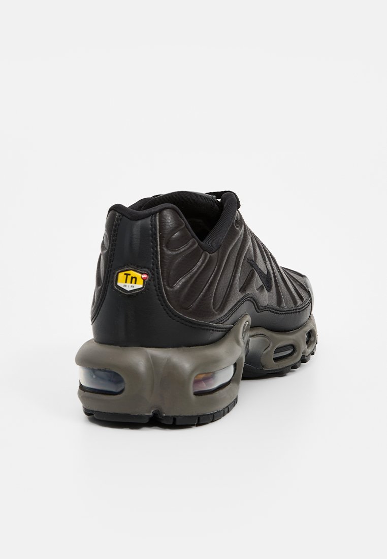 Zapatilla deportiva negra con parte superior de cuero texturizado, cuello acolchado y marca Tn Air. Presenta una suela gruesa y blanda con bolsas de aire visibles.