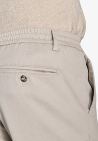 Beige afslappede bukser med elastisk talje, en baglomme med knap og sidelommer lavet af letvægtsstof.