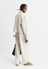 Lichtbeige denimjack met een kraag en zakken, gecombineerd met een broek met brede pijpen. Tan schoenen met ronde uitsparingen maken de outfit compleet.
