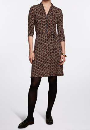Black dress with colorful paisley pattern, V-neck, three-quarter sleeves, waist tie, above-knee length, worn with black leggings and loafers.