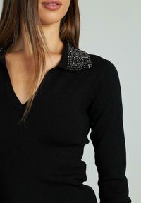 Schwarzes Strickoberteil mit V-Ausschnitt und einem strukturierten Kragen mit schwarzen Verzierungen. Elegantes, eng anliegendes Design mit langen Ärmeln.