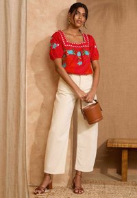 Top rosso ricamato con scollo quadrato, pantaloni larghi crema e borsa a secchiello marrone. Presenta maniche a palloncino e una texture liscia.