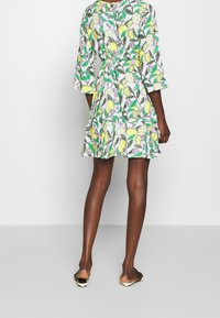 Robe florale à manches trois-quarts, avec des motifs de citrons et de feuilles jaunes et verts sur fond blanc. Design de jupe évasée.