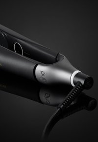 Lisseur de cheveux noir avec une pointe argentée, présentant un design élégant, des bords arrondis et un câble texturé, se réfléchissant sur une surface sombre.