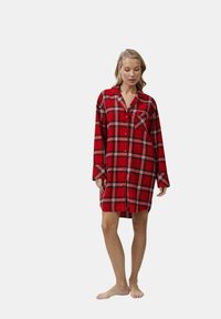 Camicia da uomo a quadri rossi in flanella con maniche lunghe, chiusura a bottoni e taschino sul petto. Presenta dettagli a scacchi bianchi e neri su tutta la superficie.