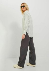 Camisa de rayas verde claro y blanca de estilo oversize, pantalones de pierna ancha gris oscuro y zapatillas beige de suela gruesa, combinados con gafas de sol negras.