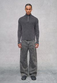 Suéter de cuello con cremallera de canalé gris sobre jeans de pierna ancha de lavado negro. El conjunto presenta texturas variadas y tonos monocromáticos. Calzado negro liso.