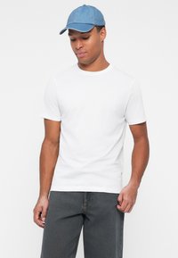 Camiseta de algodón blanca de manga corta y cuello redondo, combinada con jeans de mezclilla oscura y una gorra de mezclilla azul claro.