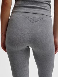 Person iført tætsiddende grå leggings og en matchende grå top, der viser bagud med en mønstret linningdetalje.