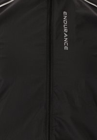 Schwarze Windbreaker-Jacke aus leichtem, strukturiertem Material mit einem Reißverschluss auf der Vorderseite. Ausgestattet mit einem weißen "ENDURANCE"-Logo und reflektierenden Akzenten.