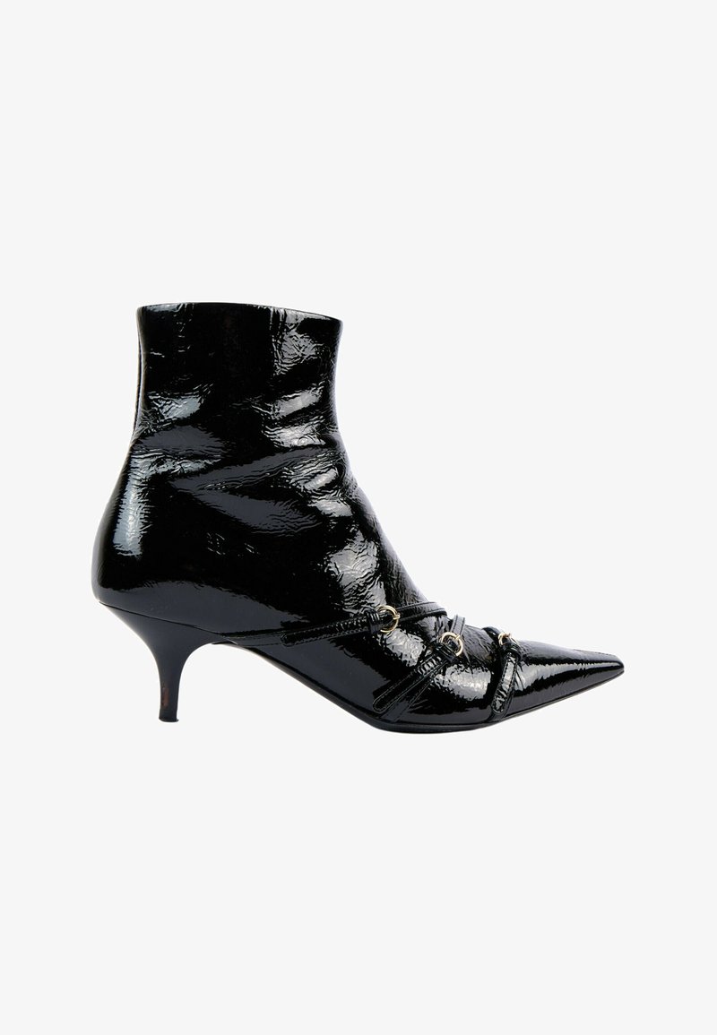 Bottine en cuir verni noir brillant à bout pointu, talon fin kitten et fines lanières décoratives avec anneaux métalliques à l’avant.