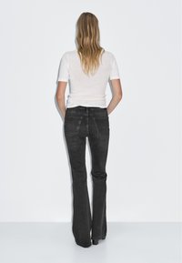 Jean flares noirs avec poches arrière, associés à une chemise ajustée à manches courtes blanche. Tissu lisse avec un léger éclat.