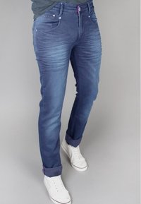 Jeans in denim blu scuro con una finitura sbiadita, caratterizzati da una texture a costine lungo le cosce, fitting slim e risvolti, abbinati a sneakers bianche.