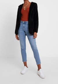Felpa nera con pelliccia e apertura frontale, indossata sopra una canotta color ruggine. Abbinata a jeans azzurri chiari e sneakers bianche.