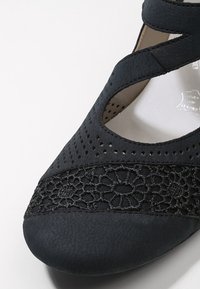 Scarpa nera con tomaia perforata, dettaglio con lacci sulla parte anteriore, punta arrotondata e design con cinturino incrociato per una vestibilità sicura.