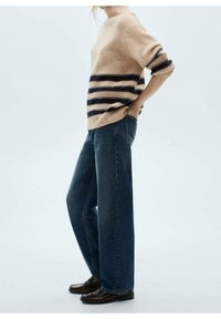 Pull rayé beige et marine, texture côtelée, avec un col haut. Associé à un jean bleu foncé à jambes larges et des mocassins marron.