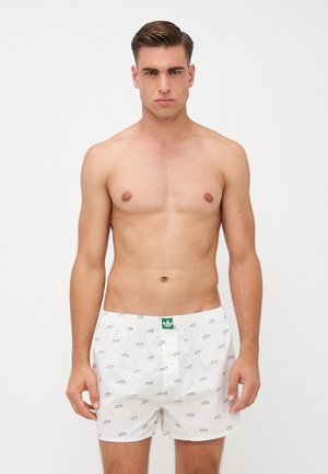 Weiße Baumwollboxershorts mit einem sich wiederholenden Sneaker-Muster, elastischem Bund und einem grünen Logolabel auf der Vorderseite. Taillierte Passform.