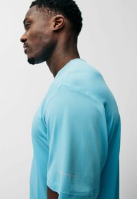 Camiseta deportiva azul claro con una tela texturizada y transpirable. Presenta un cuello redondo y mangas cortas, vista de perfil lateral.