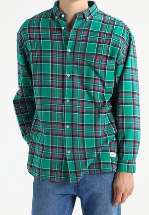Camicia a quadri verdi con bottone, dotata di taschino sul petto, bottoni bianchi e colletto classico. Il materiale ha un aspetto morbido e testurizzato.