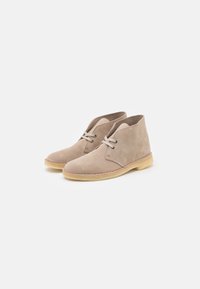 Botas de tobillo de ante beige con punta redondeada, diseño de cordones con dos ojetes y suela de goma ligera con un detalle de costura en contraste.