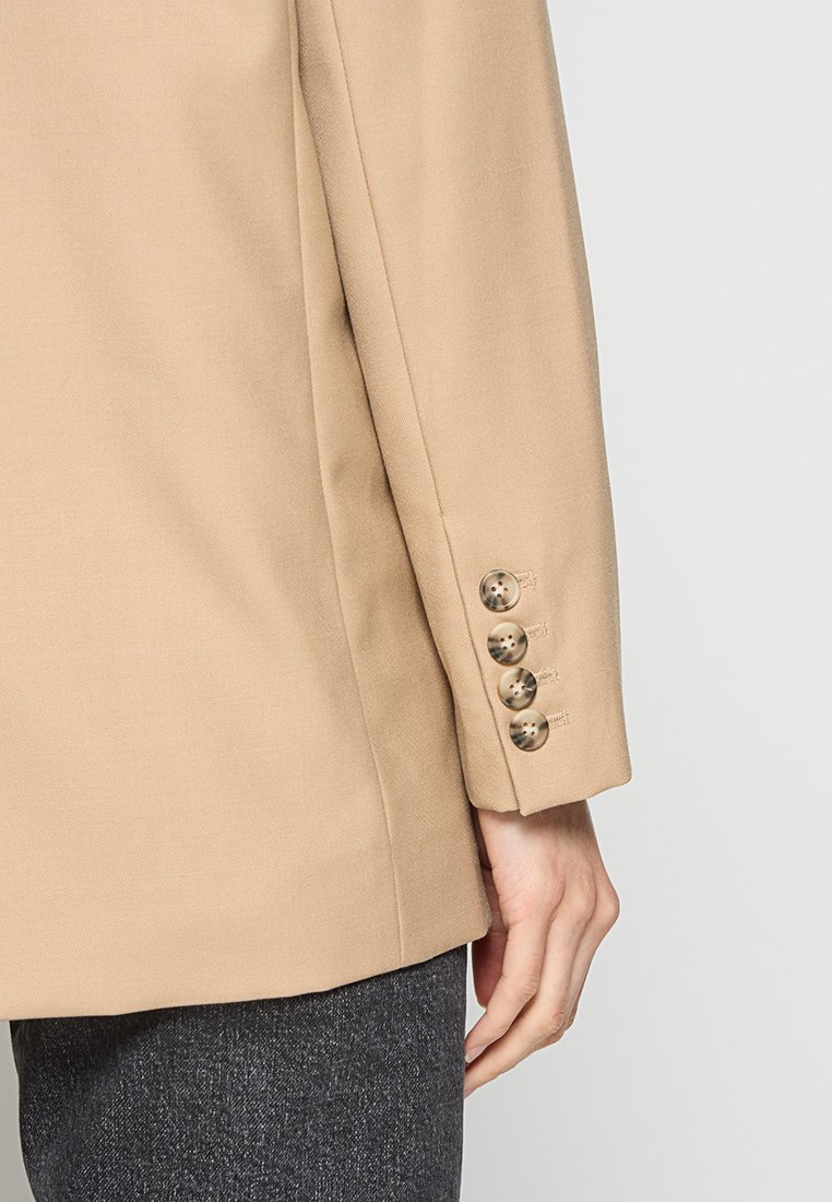 Beiger Blazer mit glatter Textur und maßgeschneidertem Schnitt, ausgestattet mit einem 5-Knopf-Manschettendetail. Der Stoff ist strukturiert und eignet sich für formelle Anlässe.