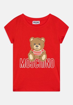 Czerwona koszulka dziecięca z krótkim rękawem, z misiem w czerwono-białej pasiastce nad napisem "MOSCHINO" w pogrubionych białych literach.