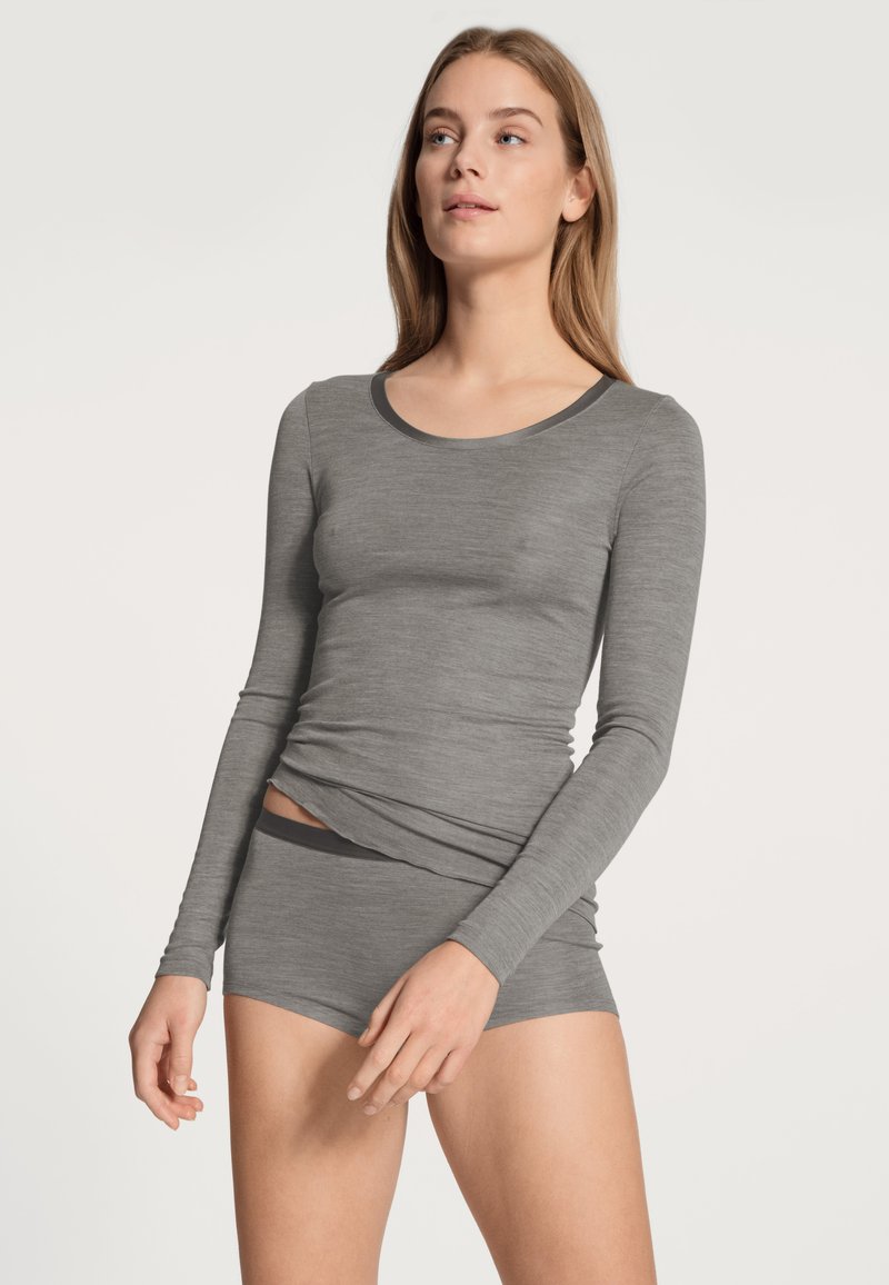 Maglia grigia a maniche lunghe con scollatura arrotondata, abbinata a pantaloni corti grigi coordinati. Il tessuto sembra morbido e aderente con una texture liscia.