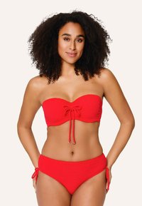 Červený bikiny set obsahuje top bez ramienok s predným viazaním a textúrovanou látkou, doplnený o zodpovedajúce spodné nohavičky so bočnými viazaniami.