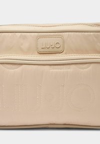 Beige steppelt táska ezüstösen fényes "LIU·JO" logóval, tónusos varrással, sima textúrával és elülső cipzáras zsebbel. Könnyű, minimalista dizájn.