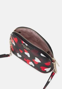 Borsa a tracolla nera con motivi a cuore rossi e bianchi. Finiture in oro, chiusura con zip e un interno rosa con tracolla a catena e dettagli in pelle.